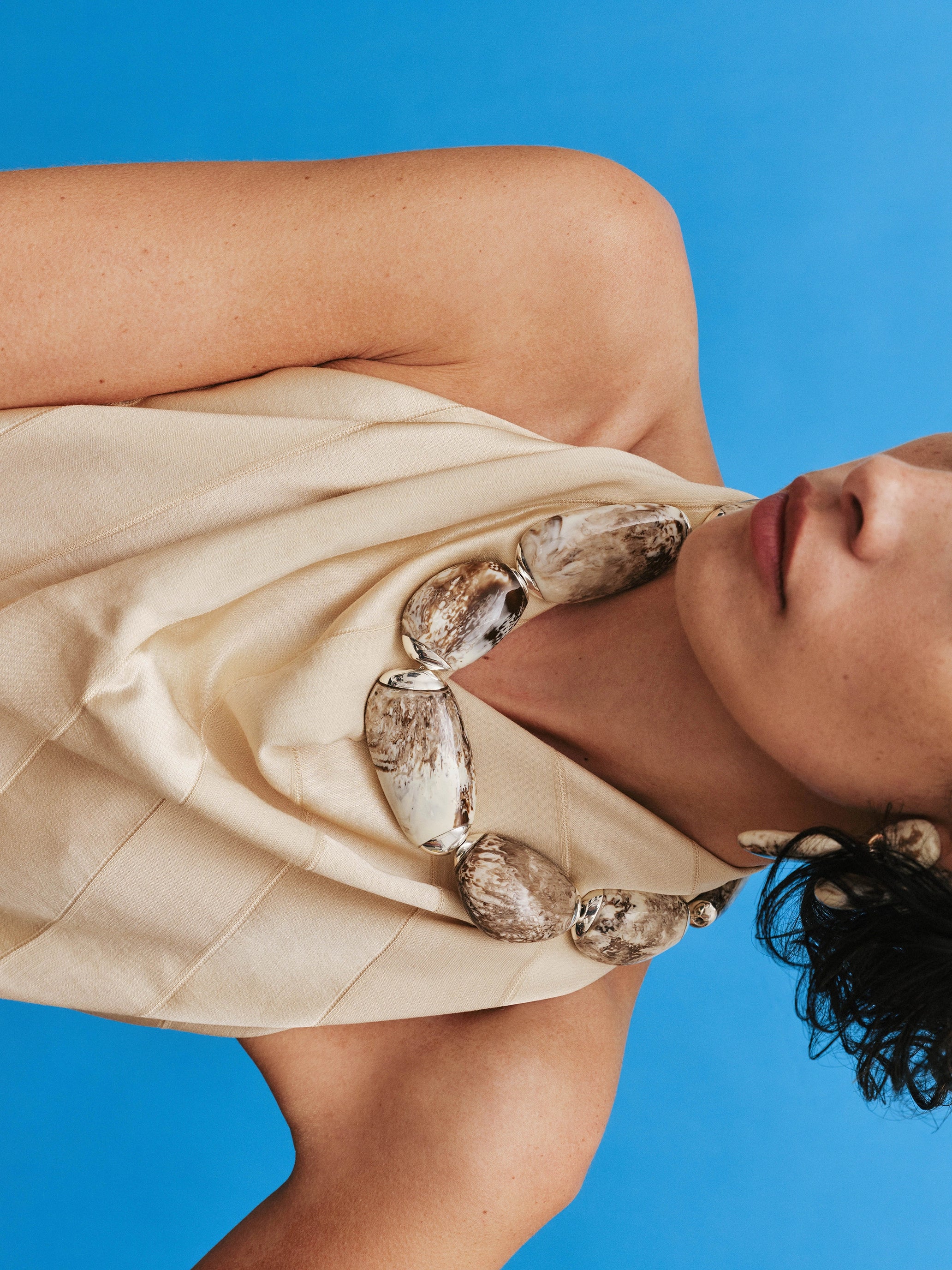 Woman wearing a beige dress with brown and silver choker against a blue background