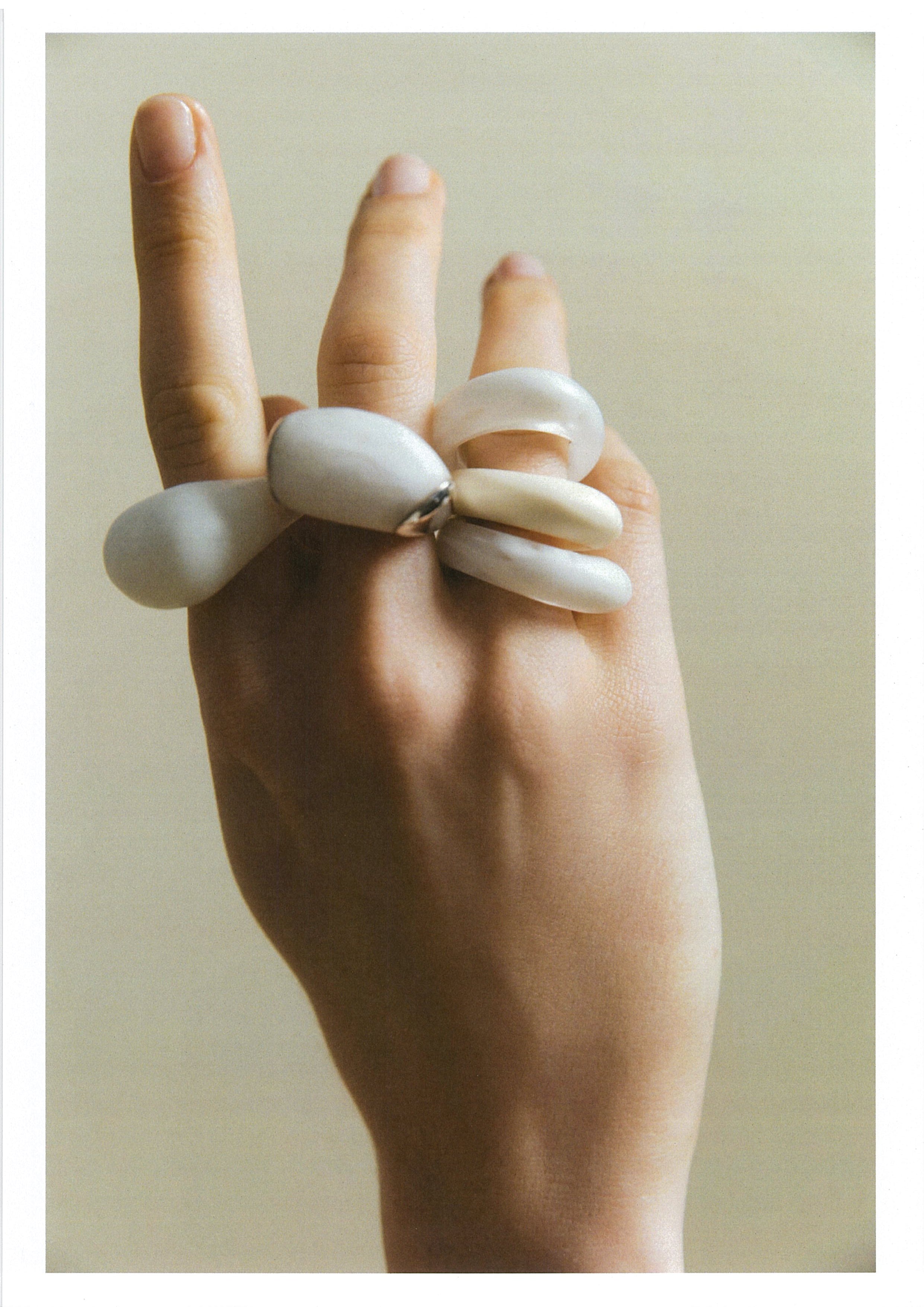 Hand wearing multiple white rings on a plain background