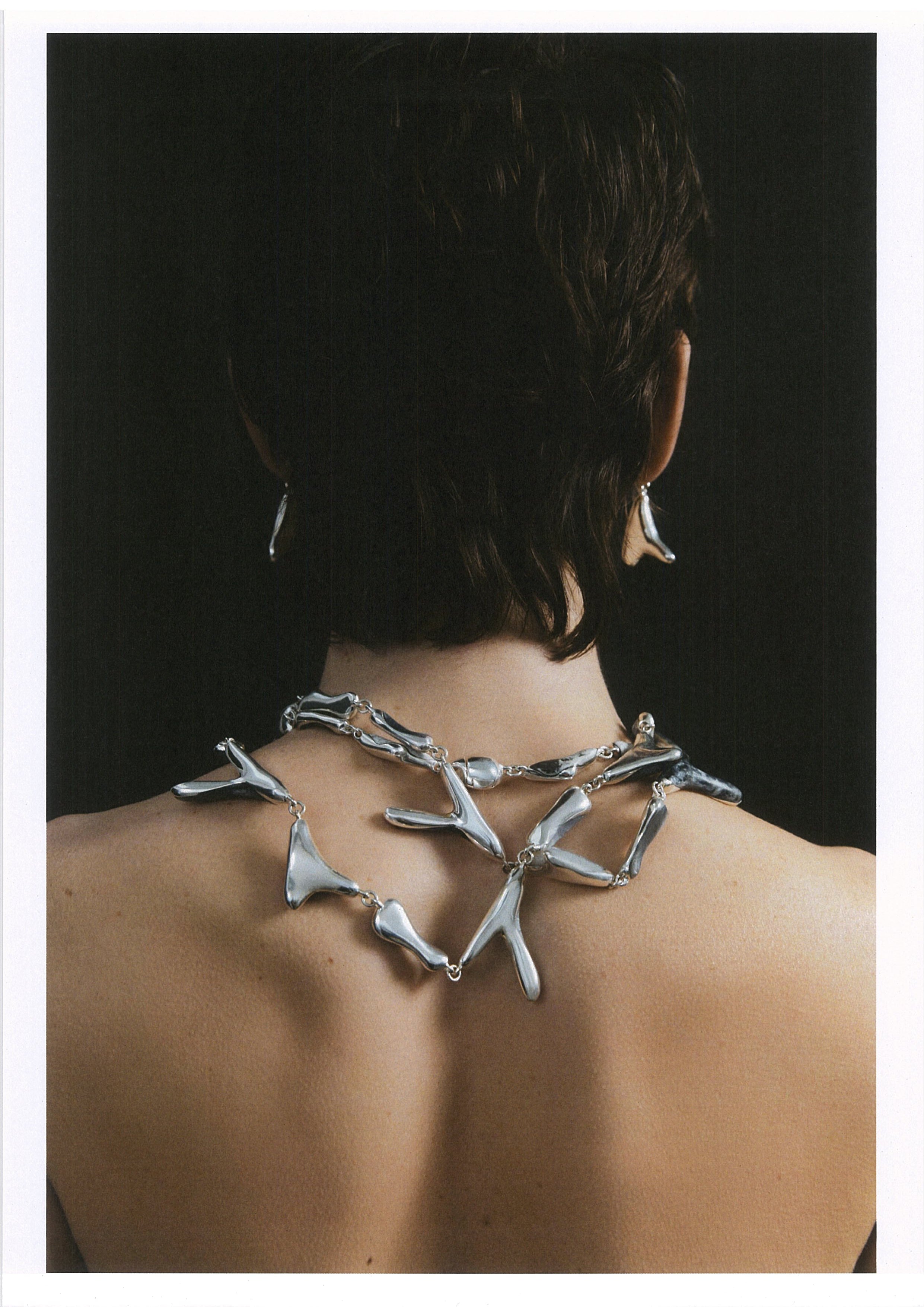 Person wearing a large, intricate silver necklace against a dark background