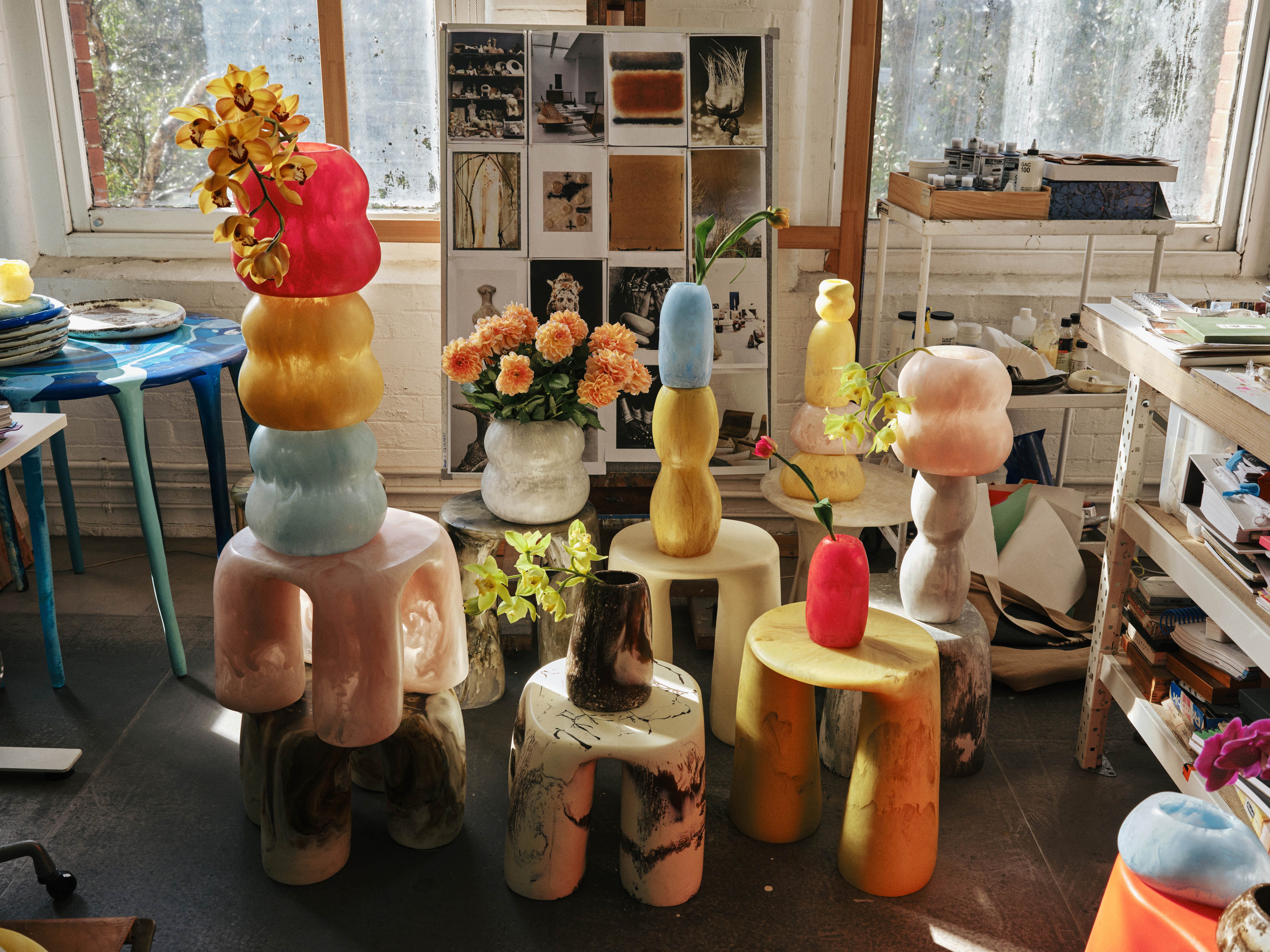 Assortment of coloured resin side tables adorned with resin vases of all sizes filled with florals in a studio space