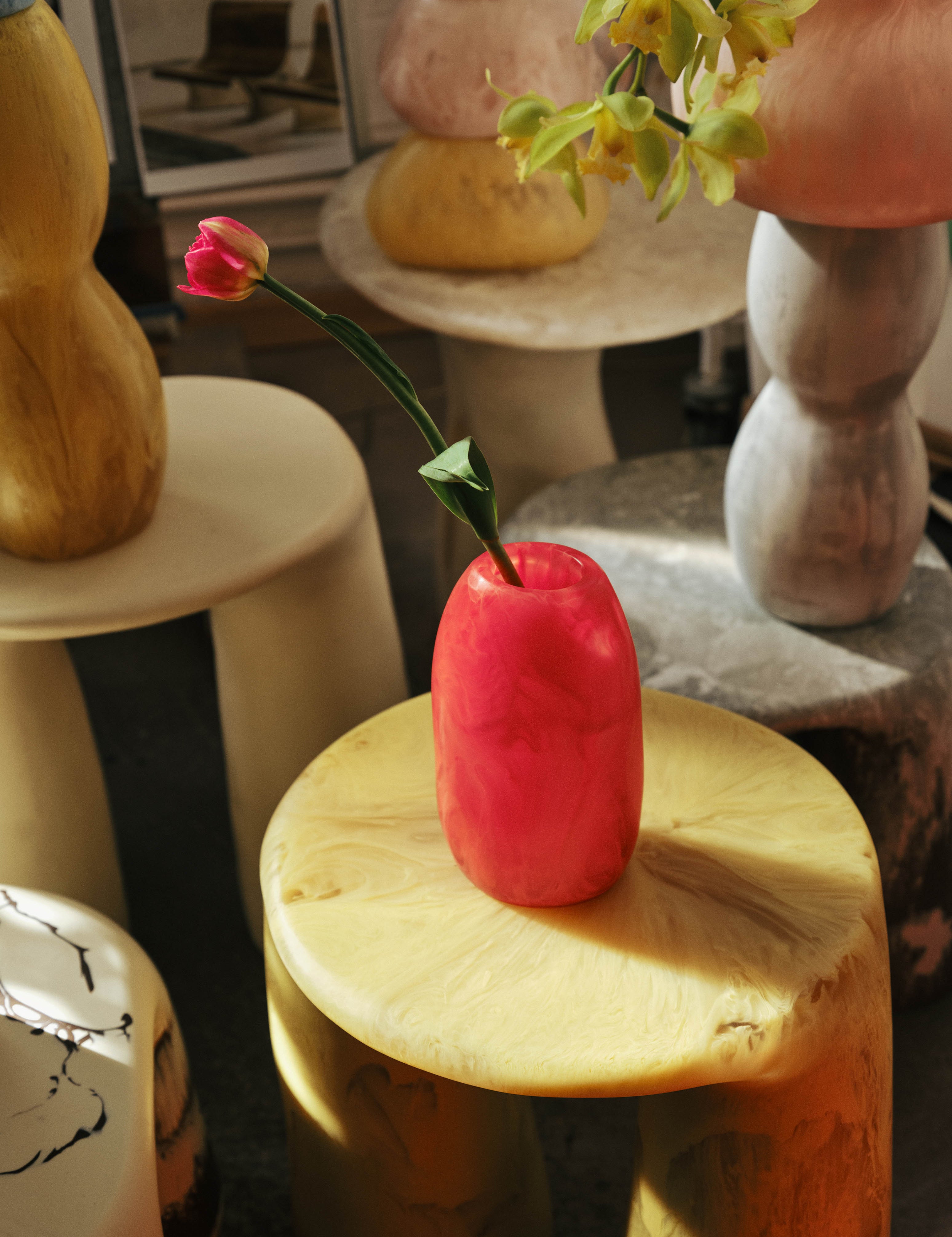 Orange tone vase with single stem flower sitting on a yellow resin side table