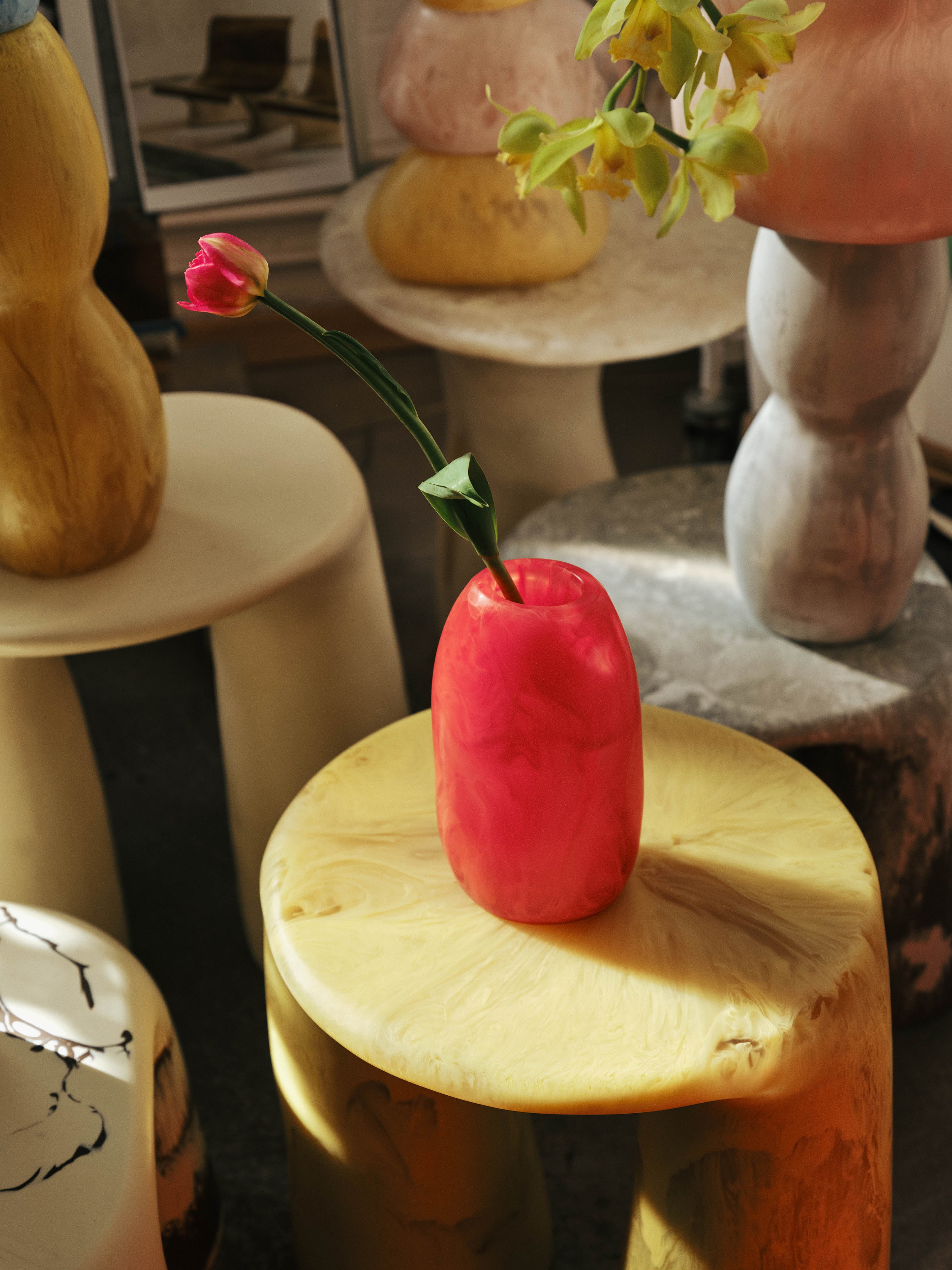 Orange tone vase with single stem flower sitting on a yellow resin side table