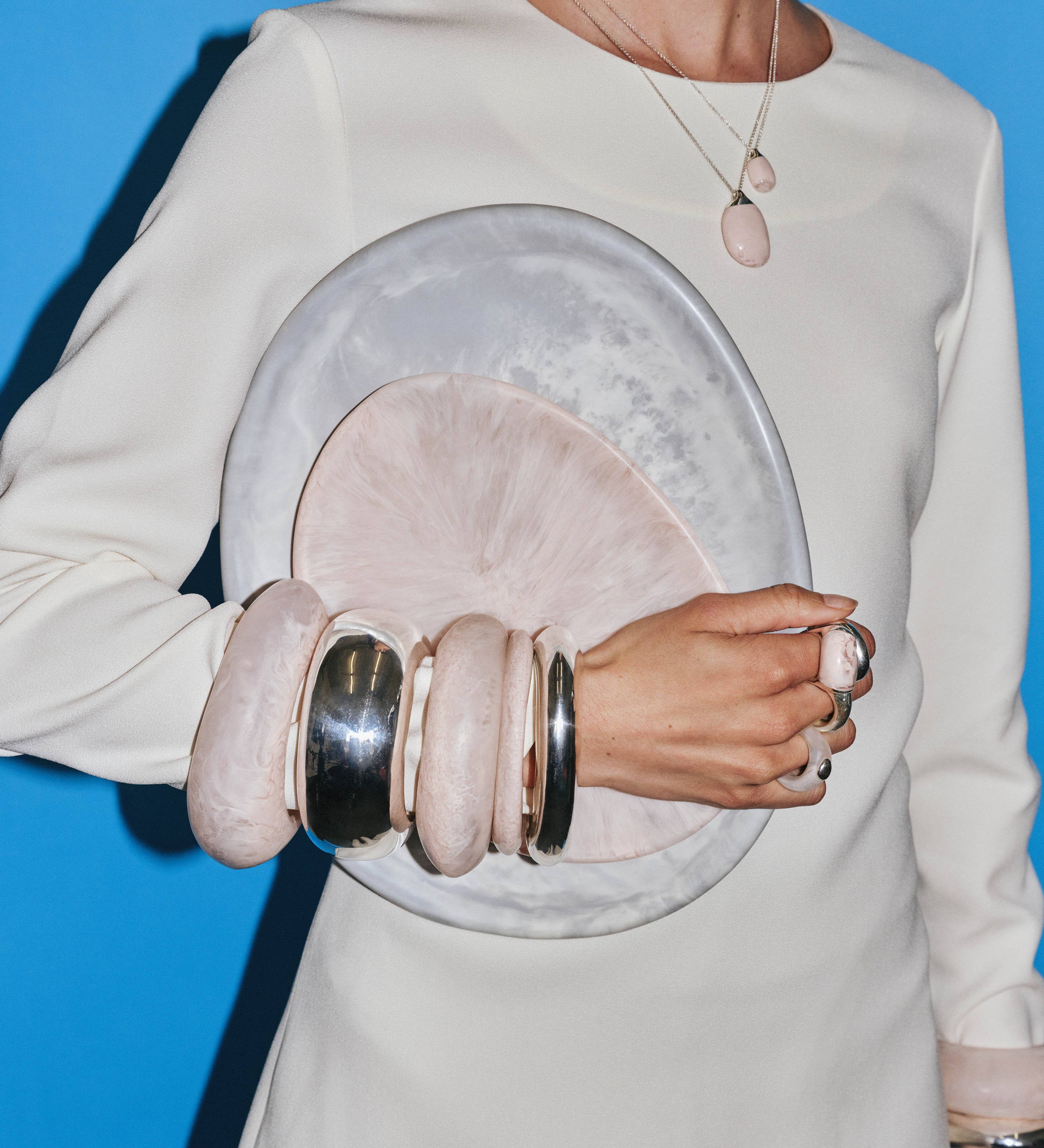 Model wearing assortment of pink and silver bangles, holding a large grey plate and small pink plate