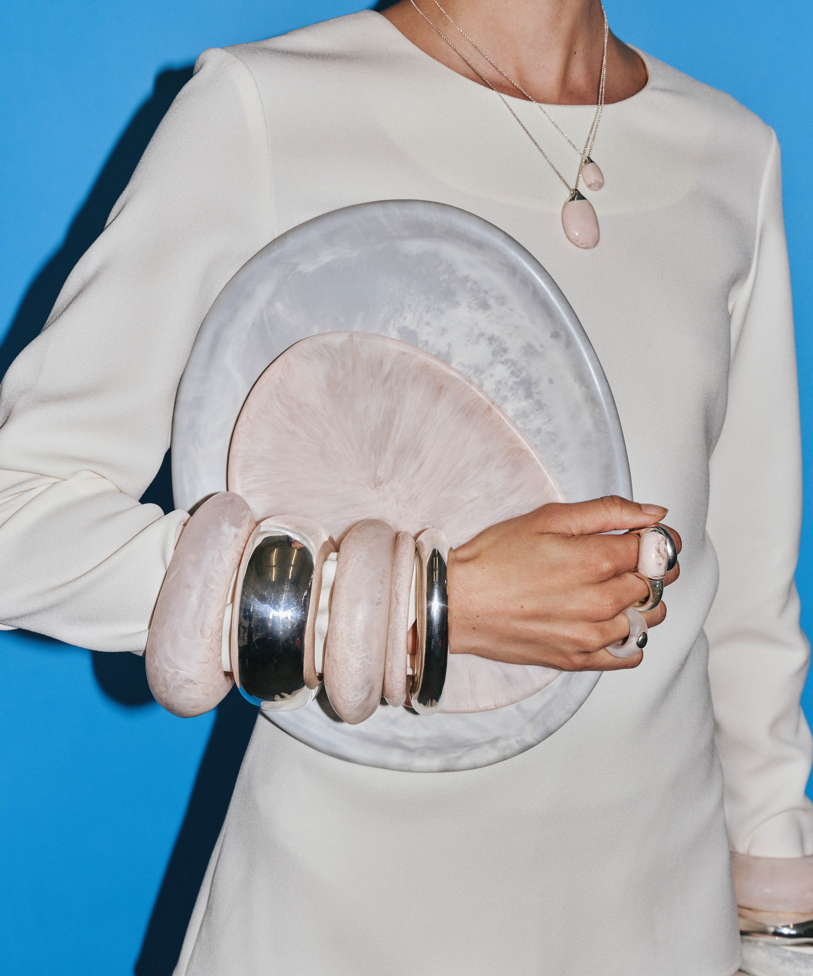 Model wearing assortment of pink and silver bangles, holding a large grey plate and small pink plate