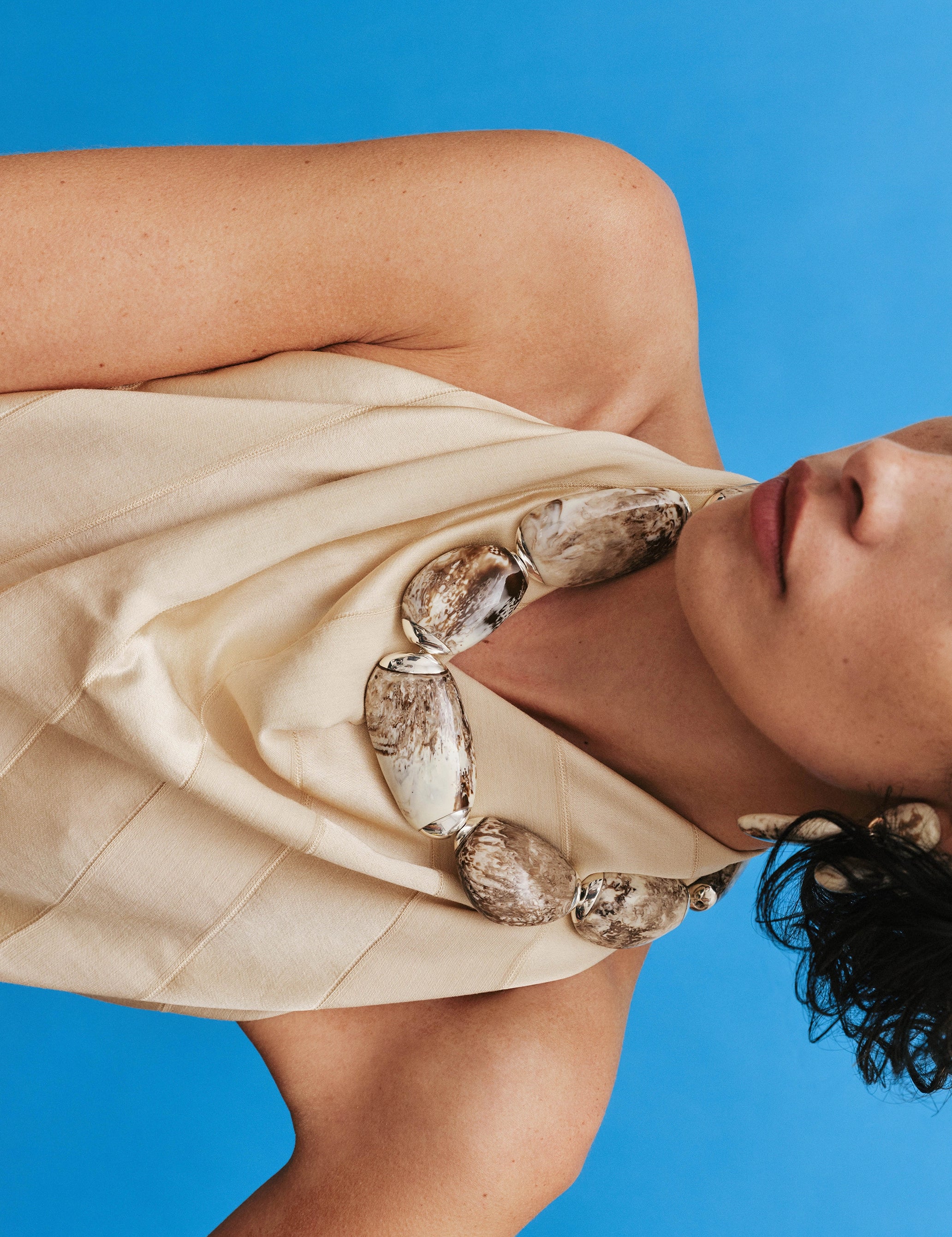 Woman wearing a beige dress with brown and silver choker against a blue background