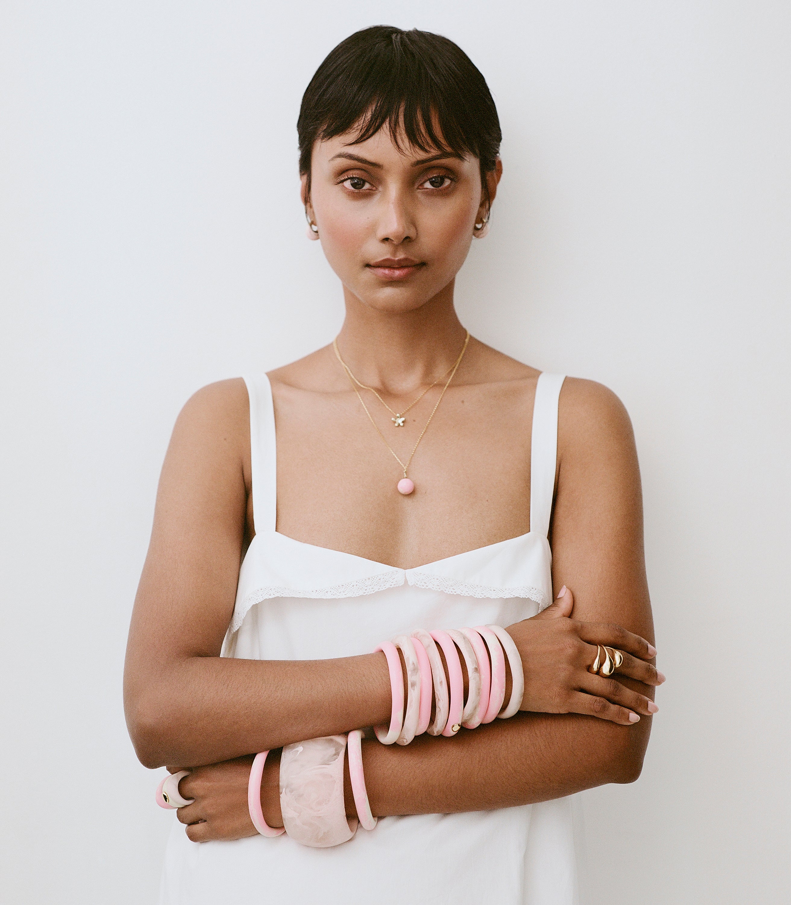 Model wearing white dress with variety of pink toned resin bangles and brass accent  rings and pendants