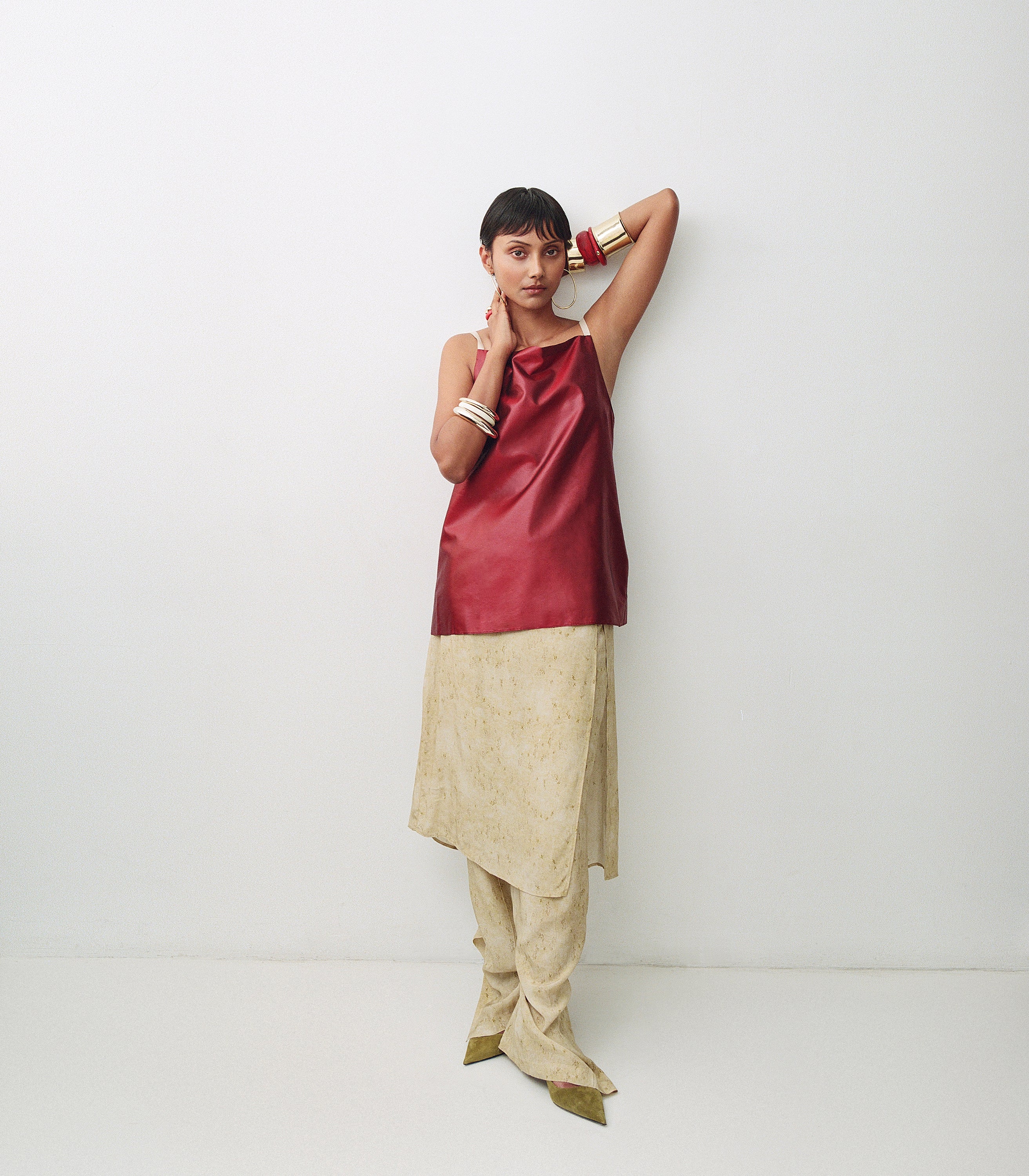 Model wearing red and beige outfit with variety of brass bangles with pink accent bangles