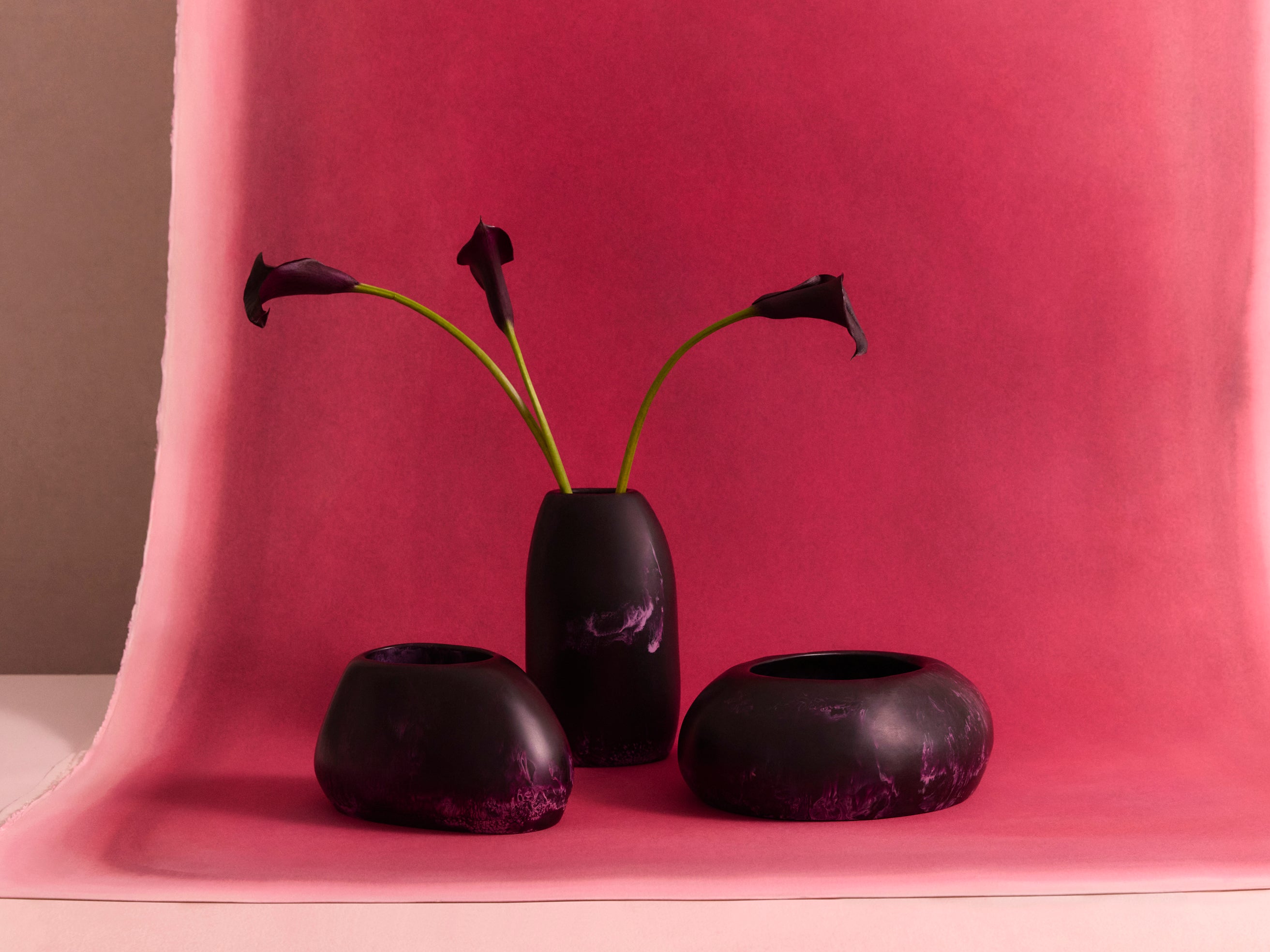 Set of three deep purple vases on a red backdrop with floral stems