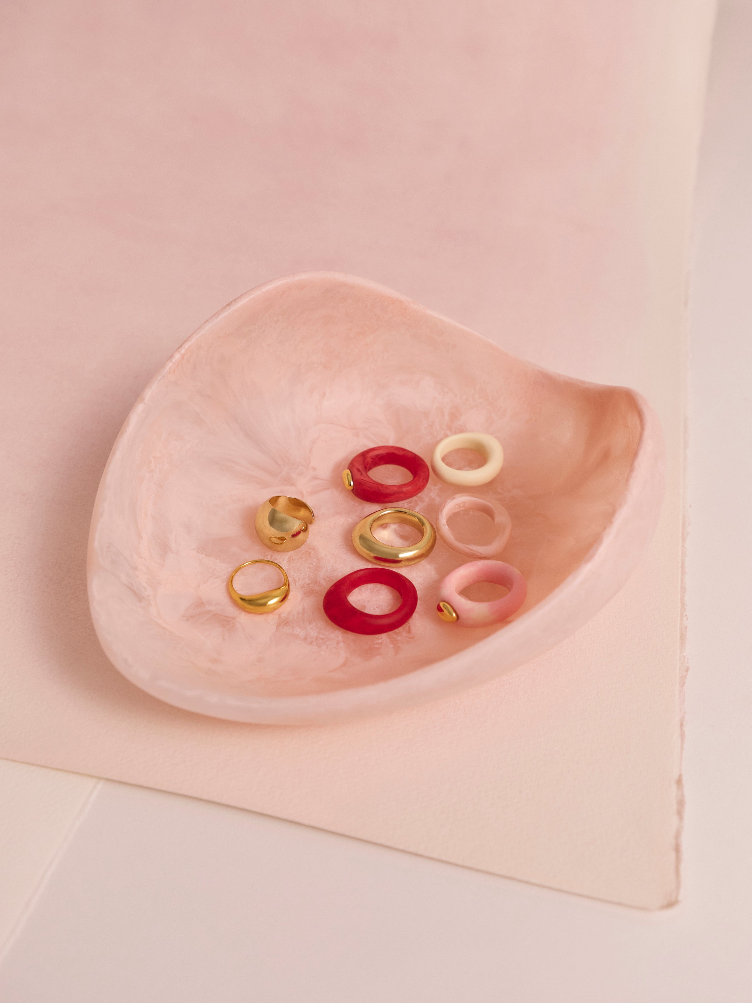 A pink resin bowl holding a variety of brass and pink resin rings