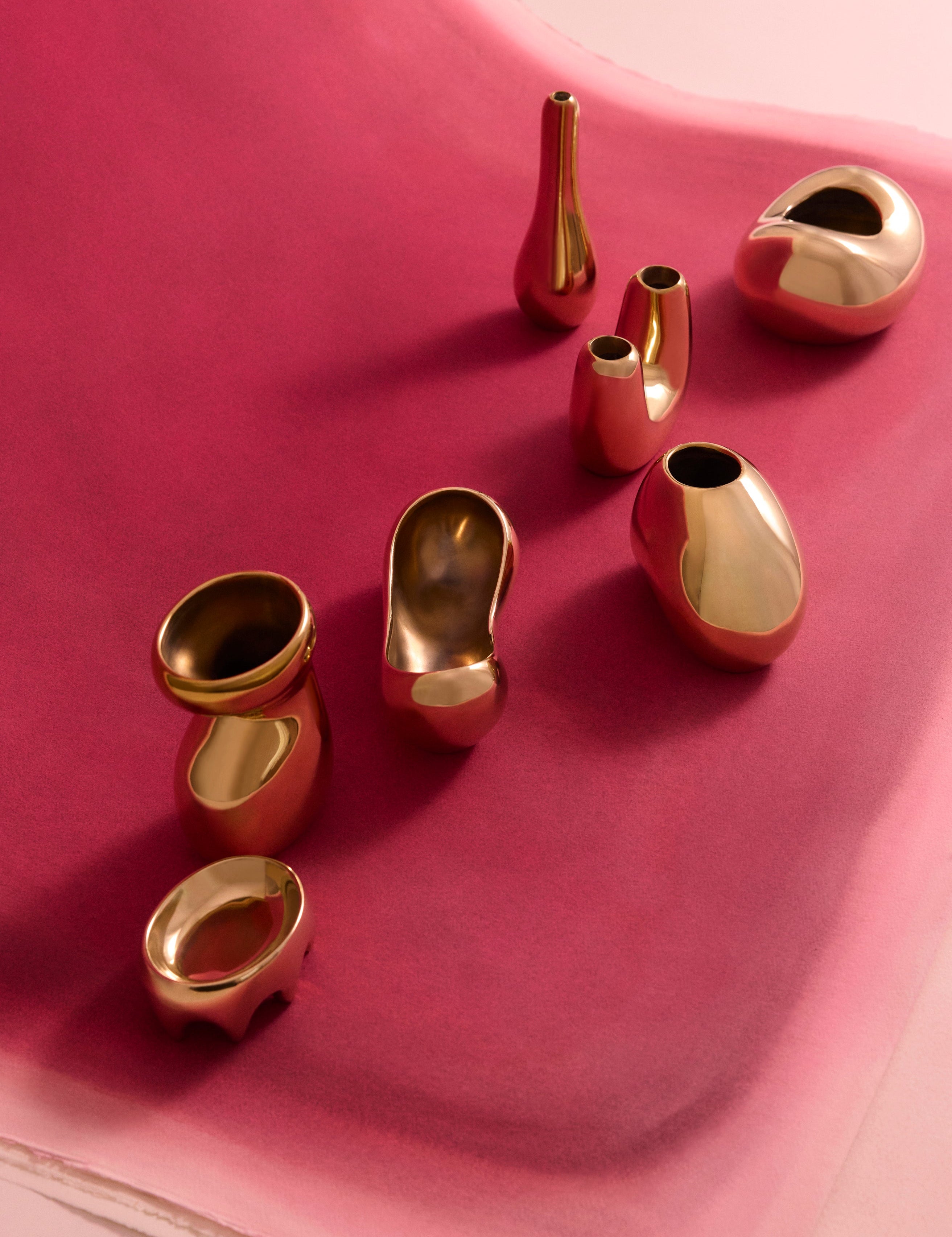 Variety of sculptural brass vases on a pink backdrop
