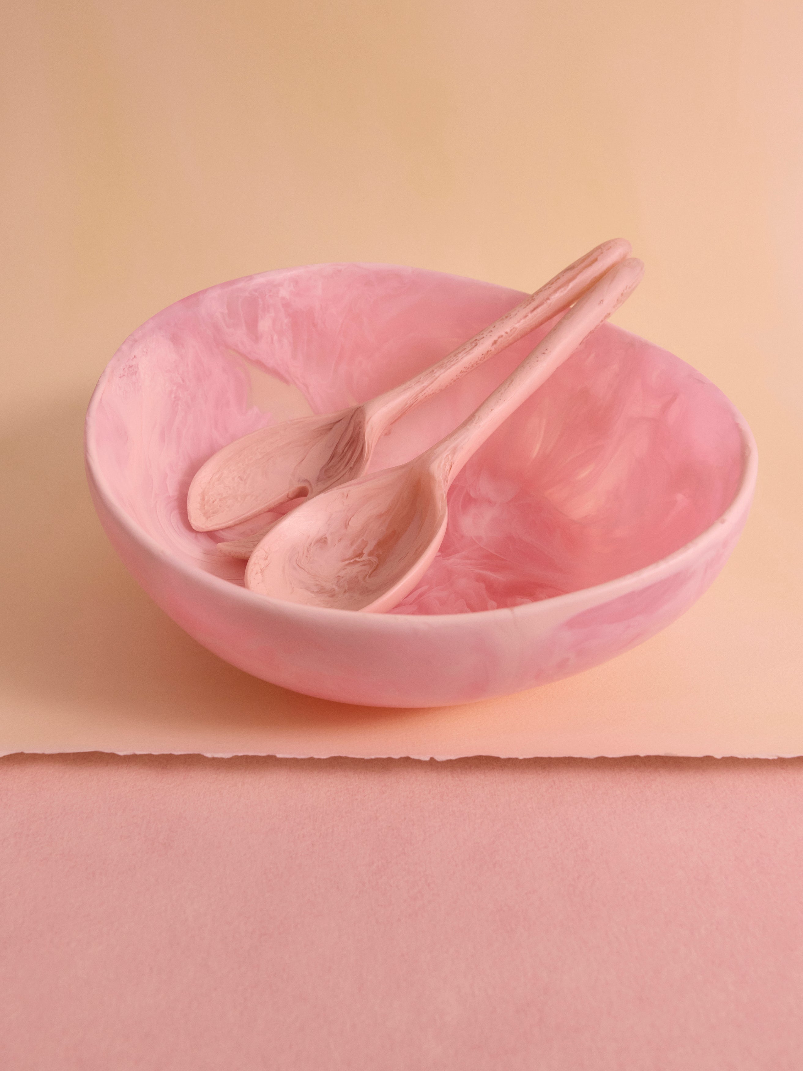 Pink salad bowl with two pink servers within, on a cream backdrop