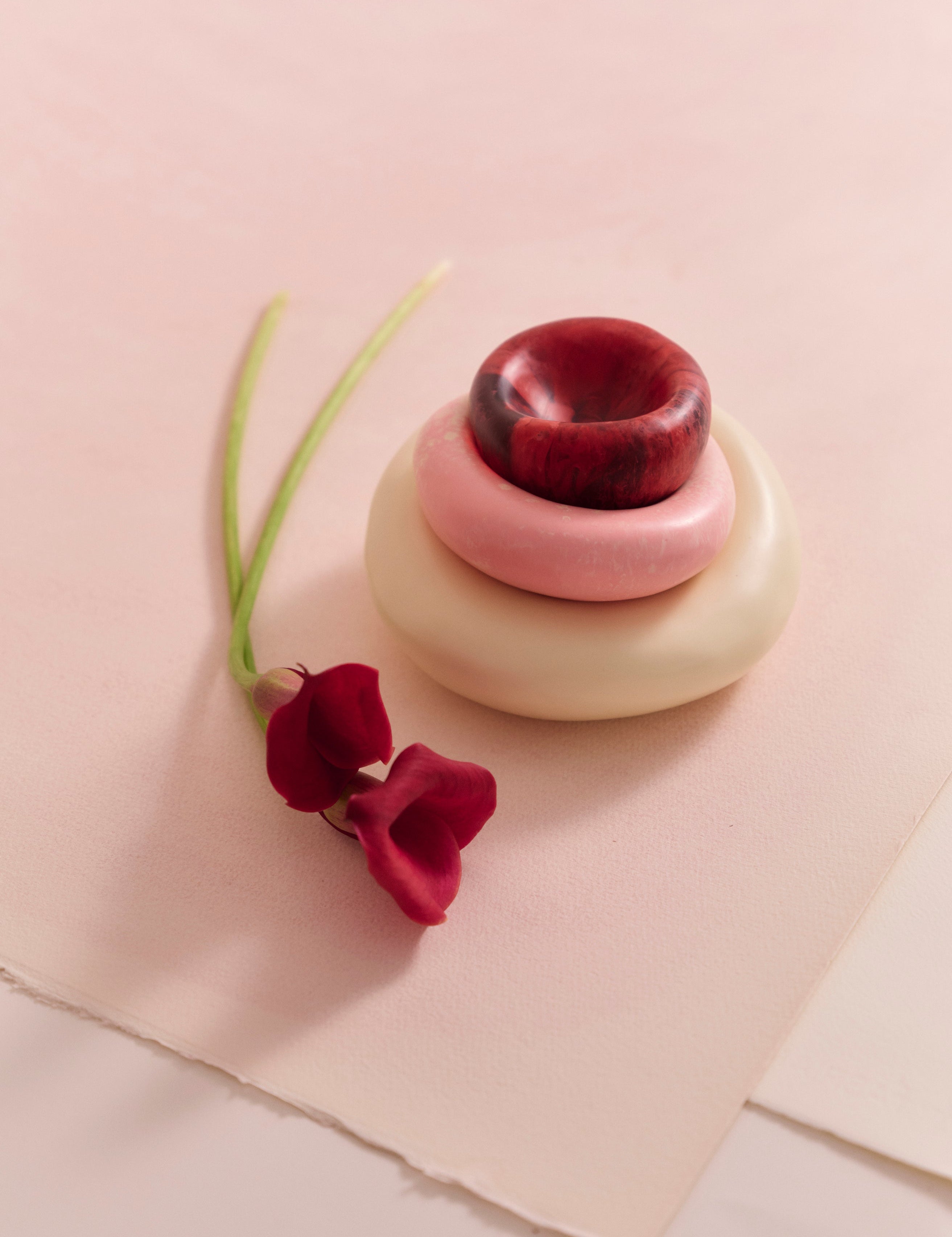 Stack of resin dishes accompanied by floral stem on a beige backdrop