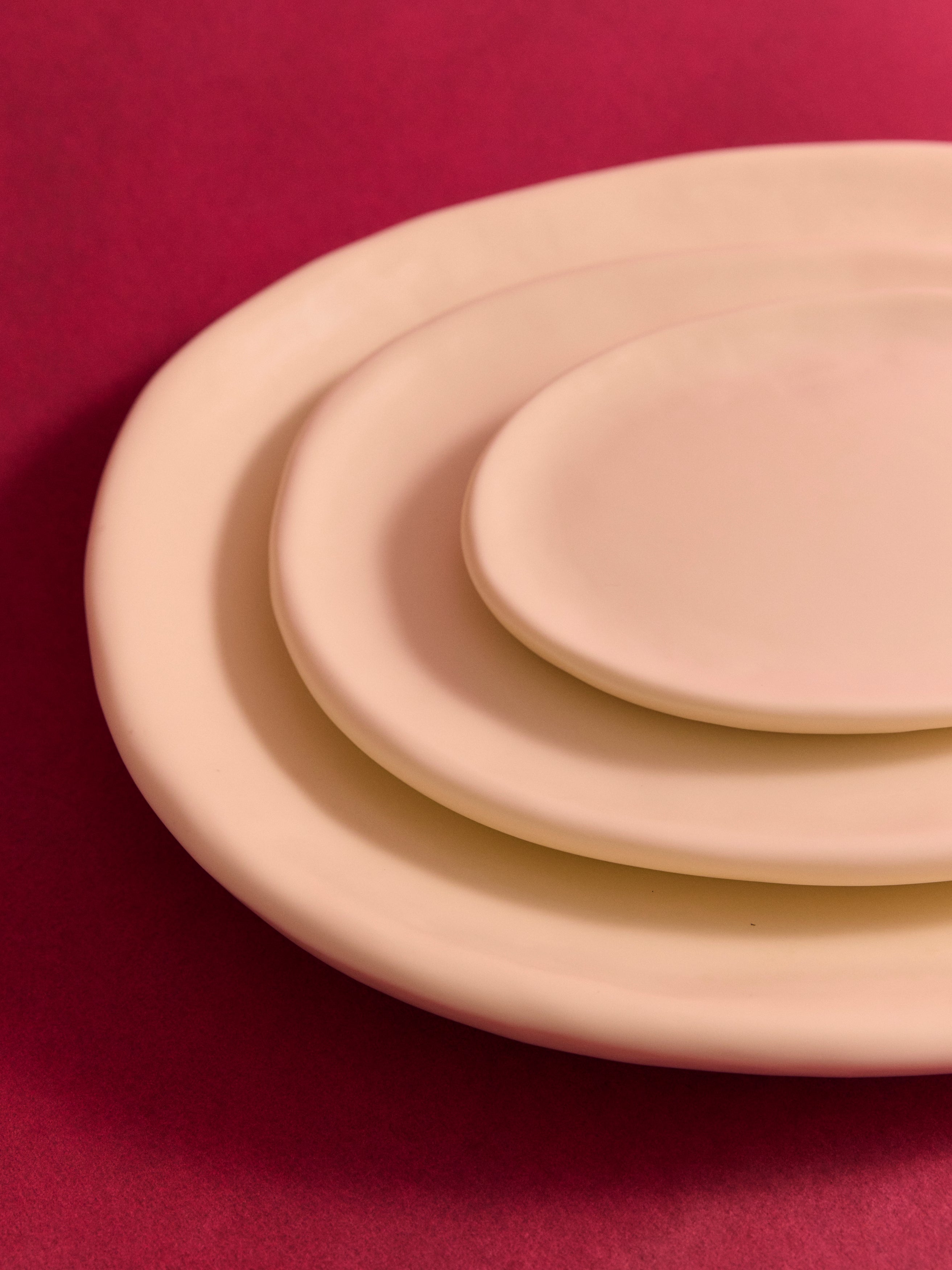Stacked cream coloured resin serving plates on a deep pink backdrop
