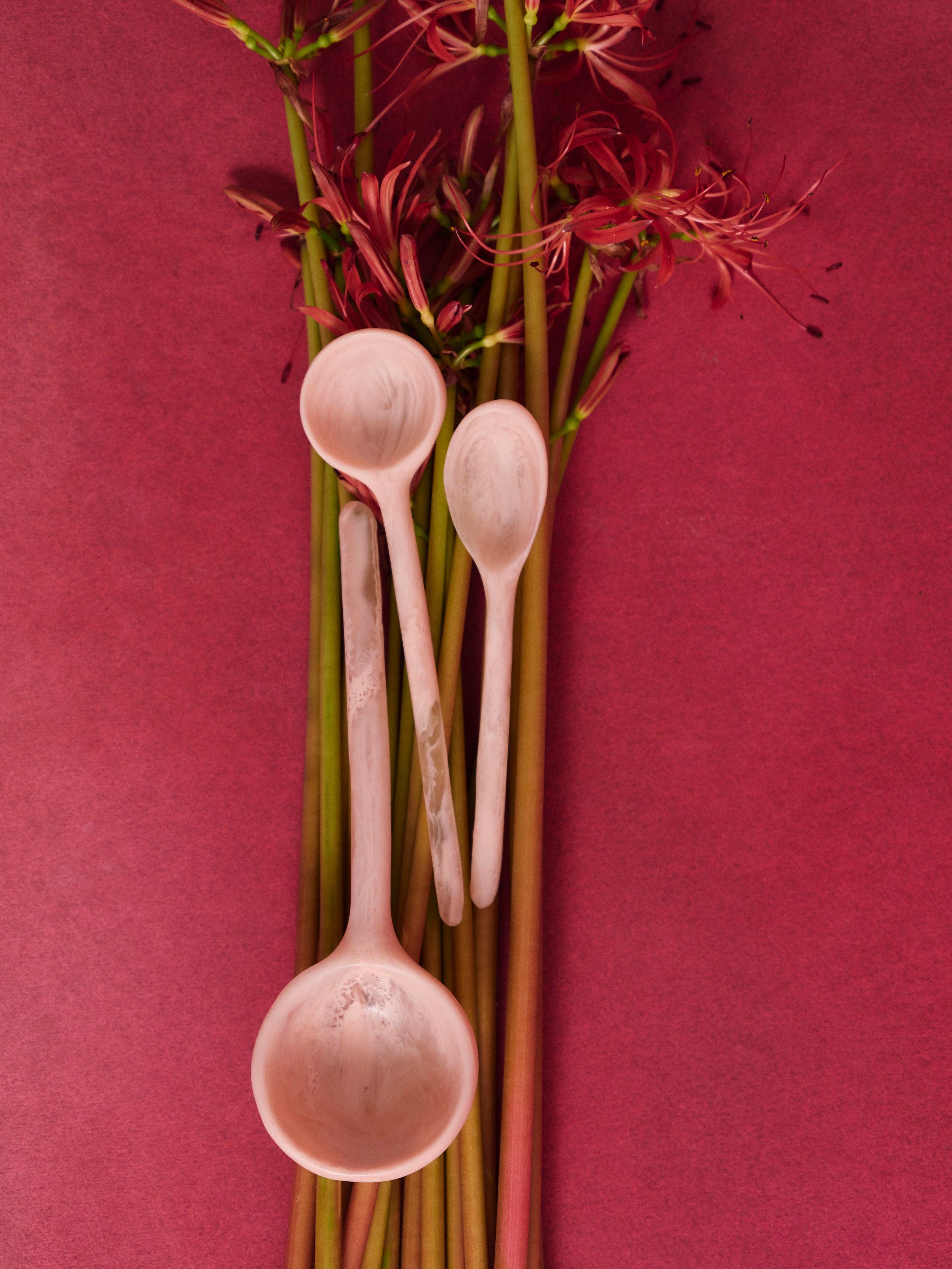 Three pink resin spoons laid upon a bunch of red flowers