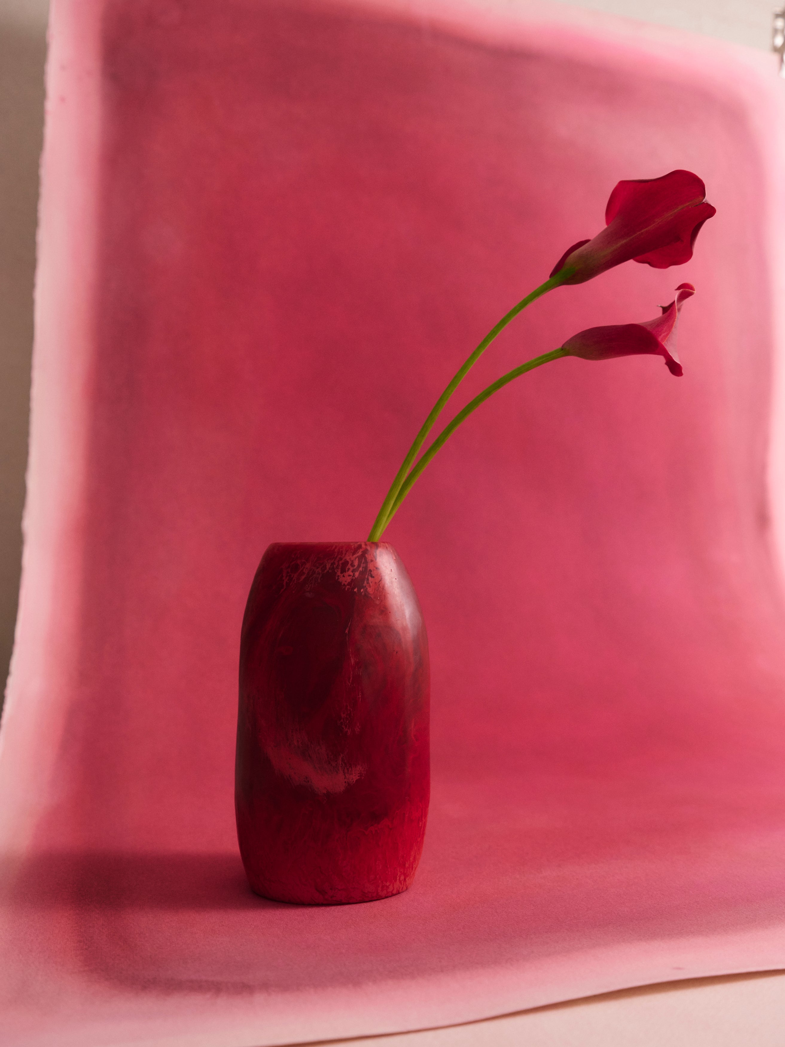 Deep pink resin vase with a single red flower against a pink background