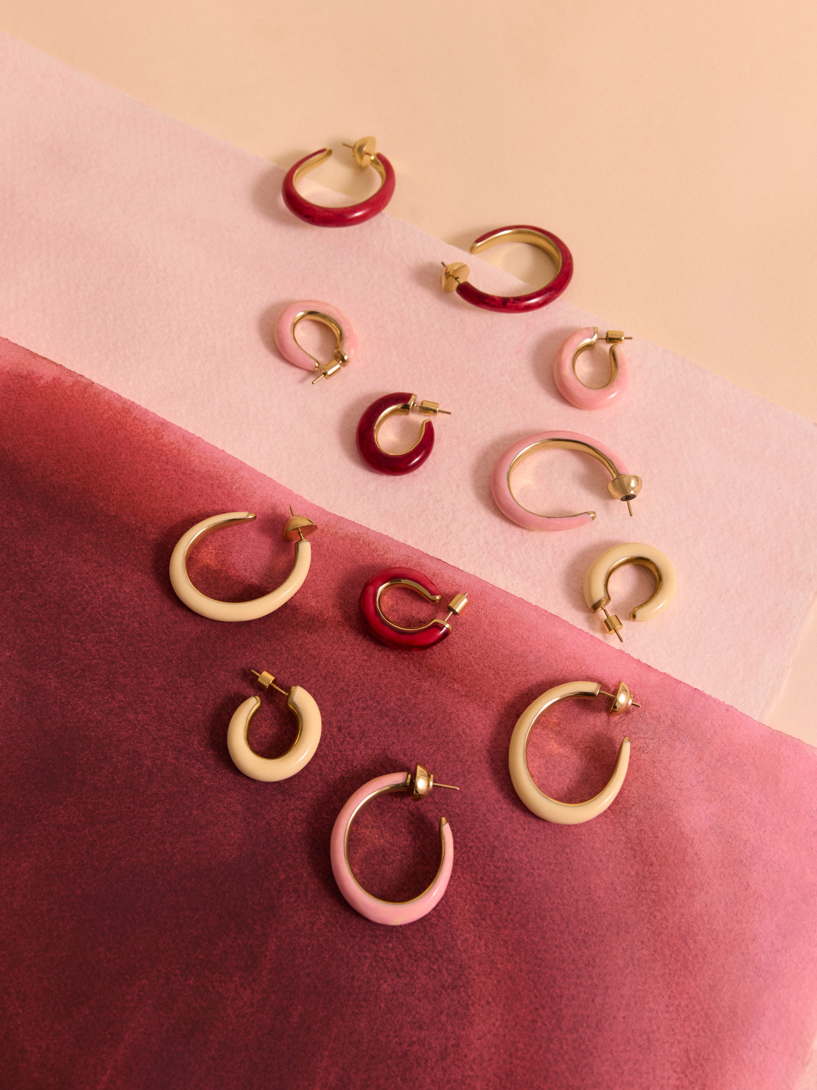 Variety of resin and brass oval hoop earrings on pink backdrop