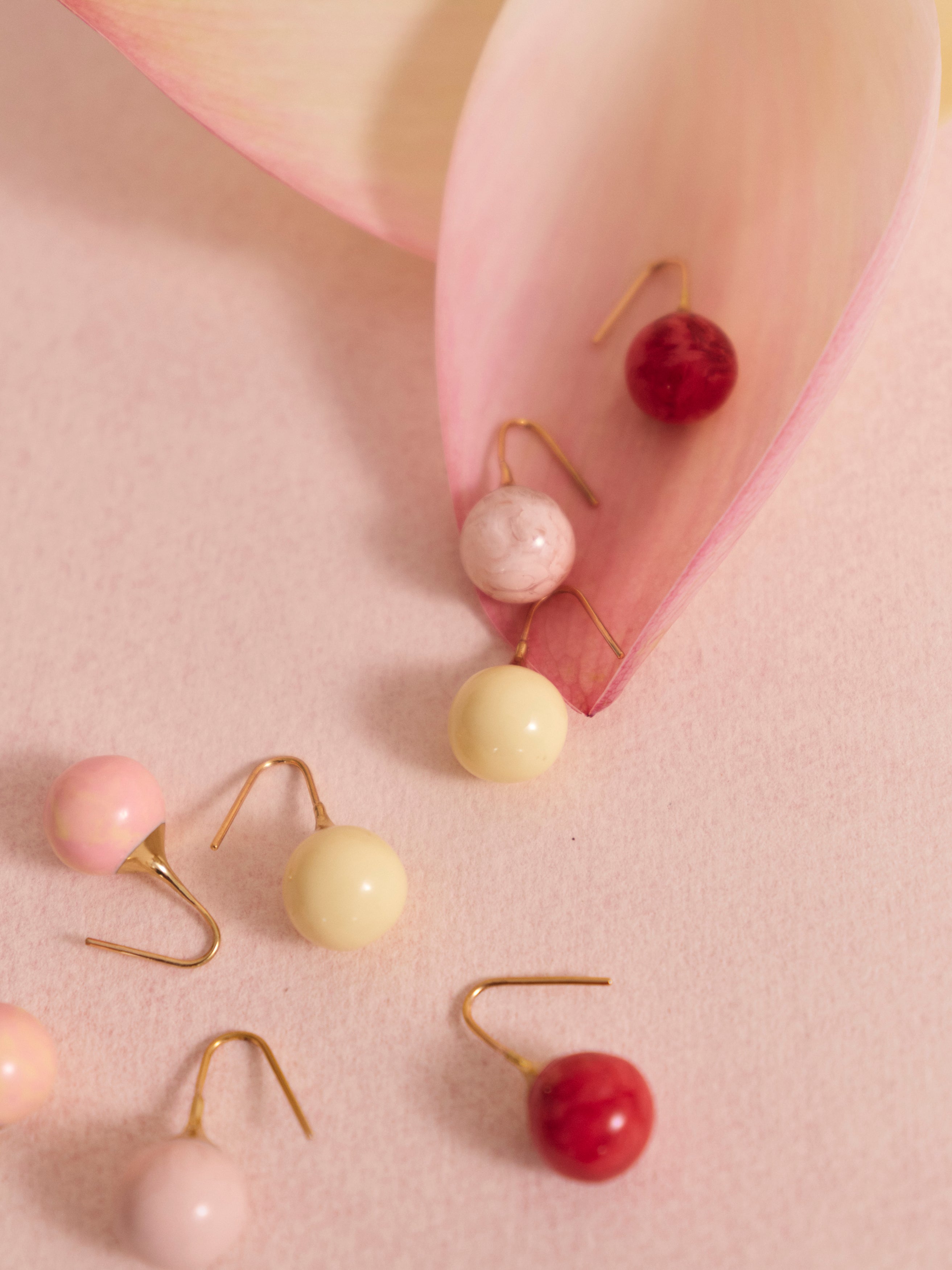 Pink and cream ball drop resin earrings in a flower petal on a pink backdrop