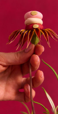 Hand holding a decorative flower with a stack of pink and cream rings with gold accents on a red backdrop