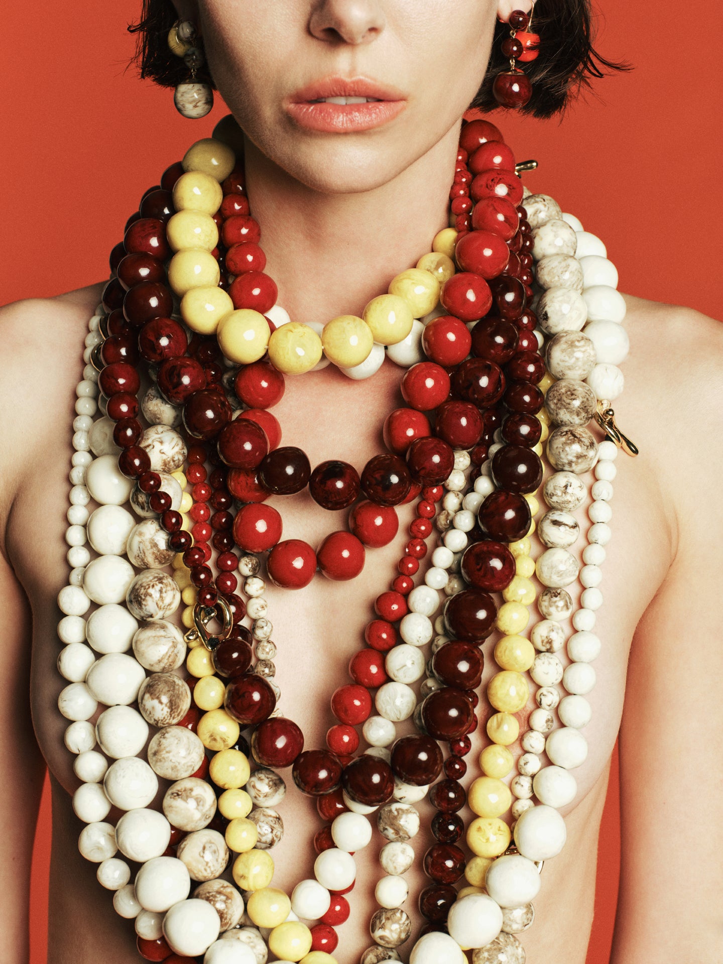 Woman wearing multiple colorful beaded necklaces against a red background