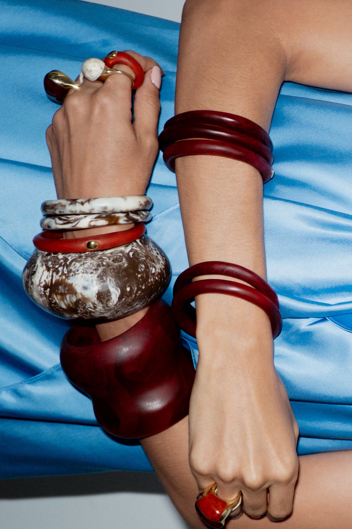 Close-up of a person's arm with multiple bracelets on a blue fabric background