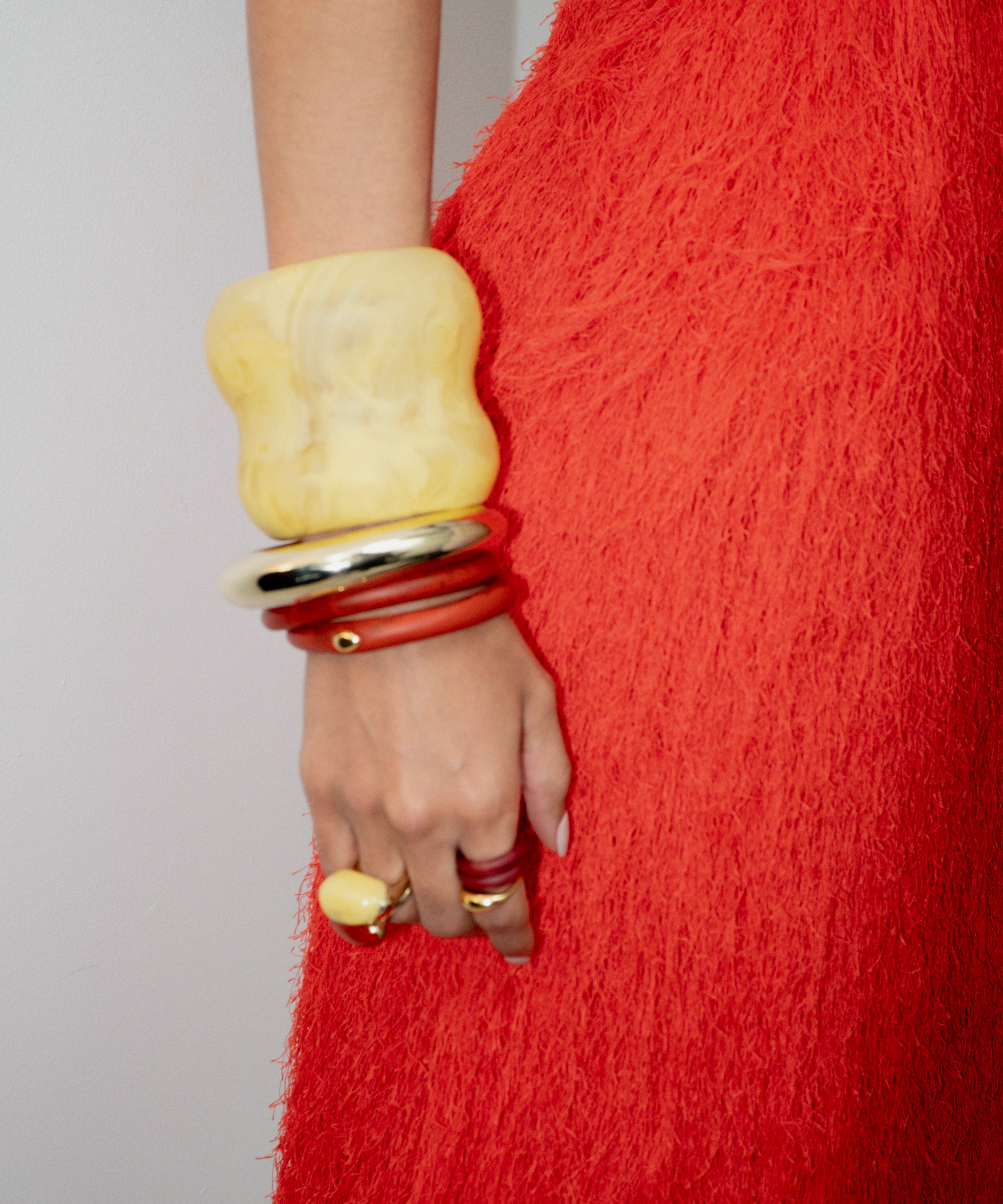 Person wearing a red textured garment with yellow and red bracelets on a plain background