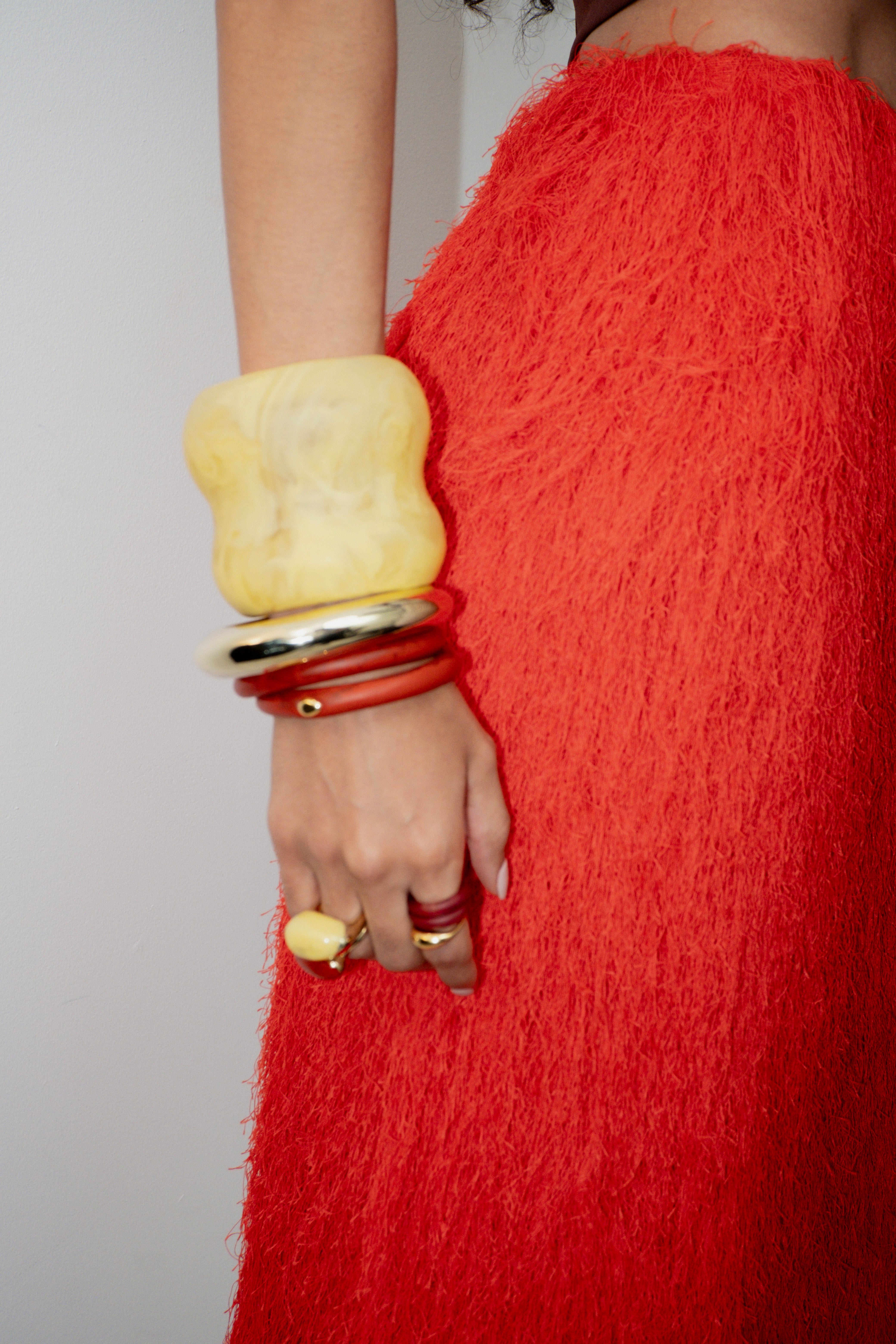 Person wearing a red textured garment with yellow and red bracelets on a plain background