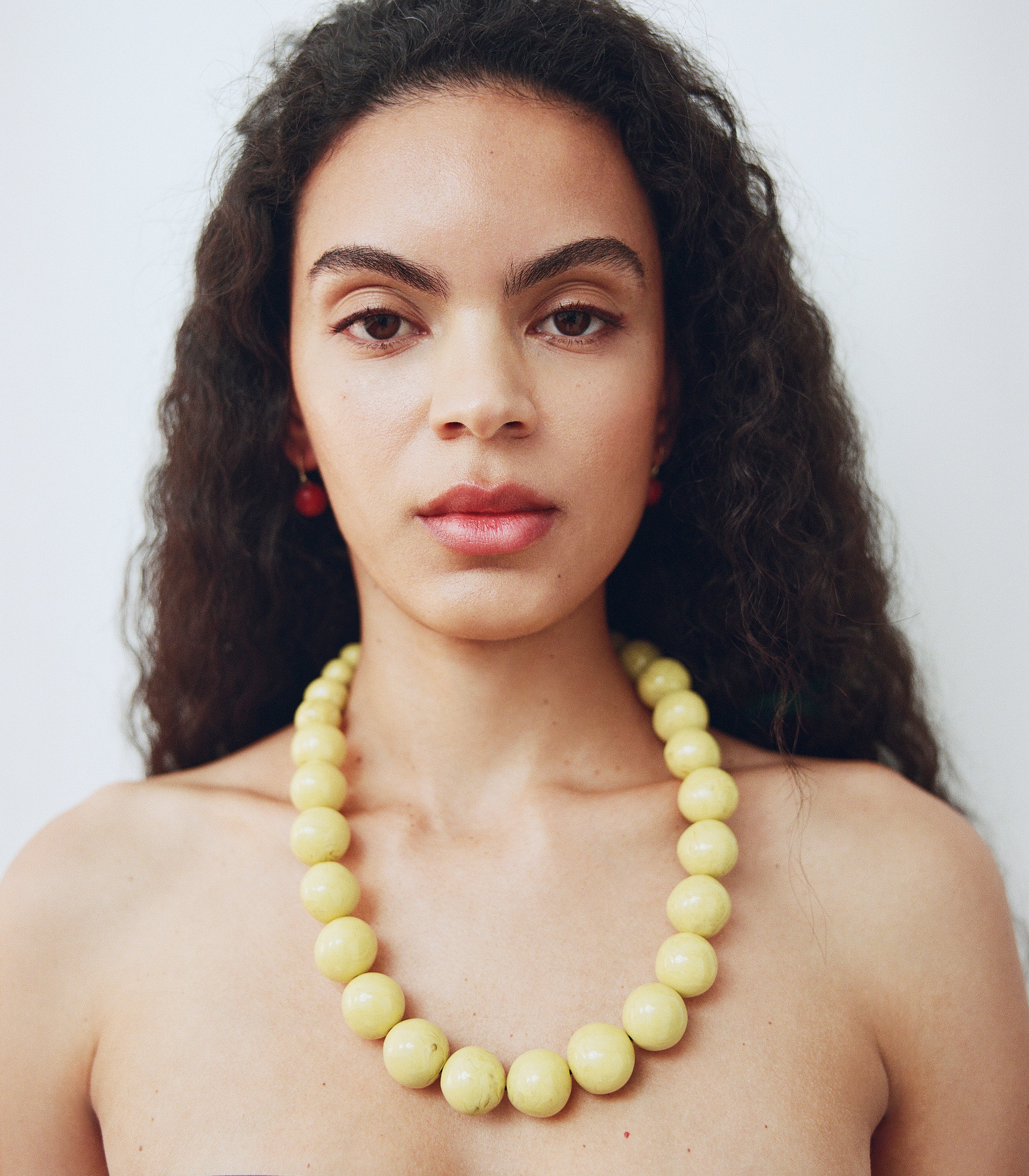 Woman wearing a yellow beaded necklace against a plain background