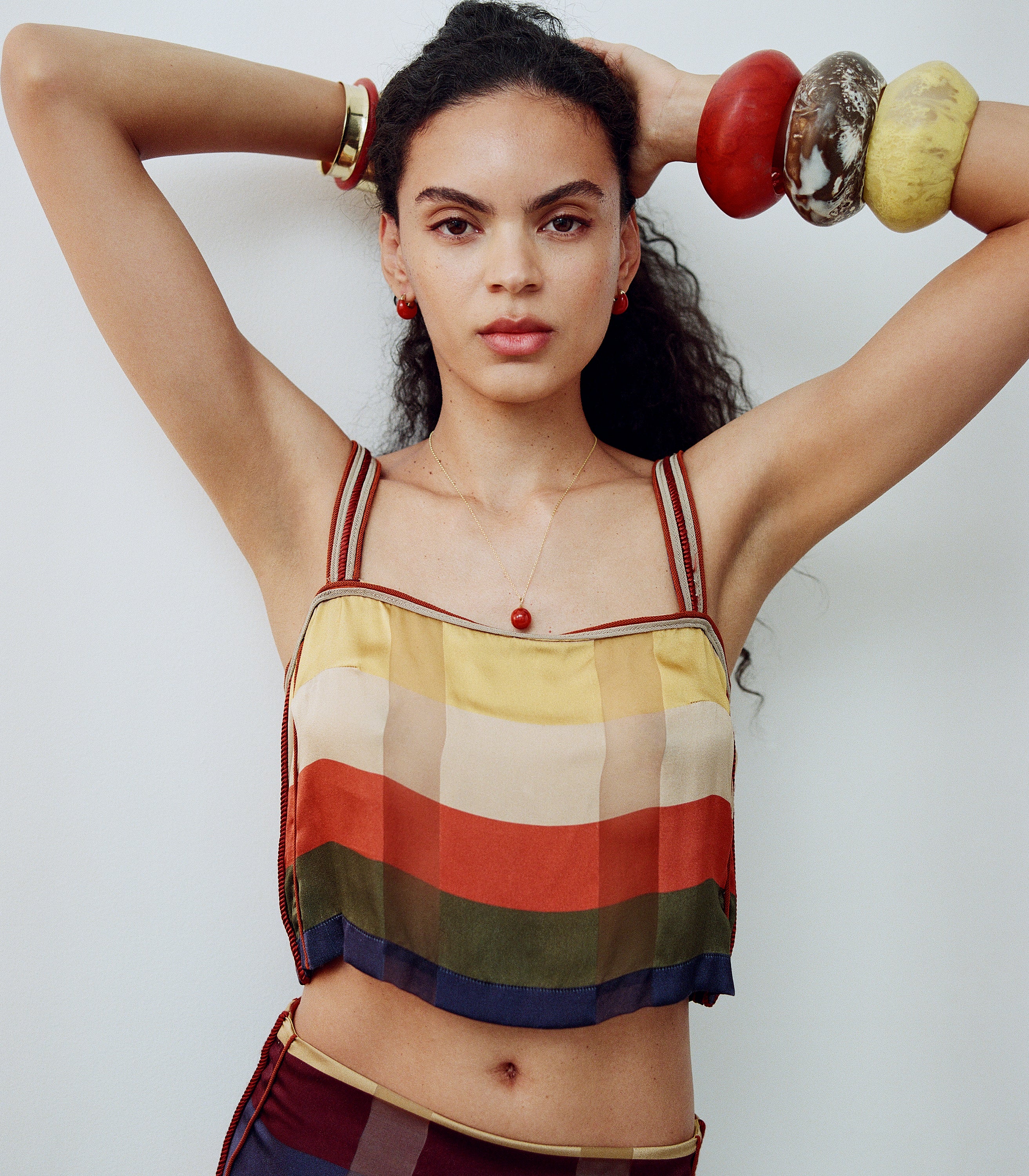Woman wearing a colorful striped top with arms raised against a white background