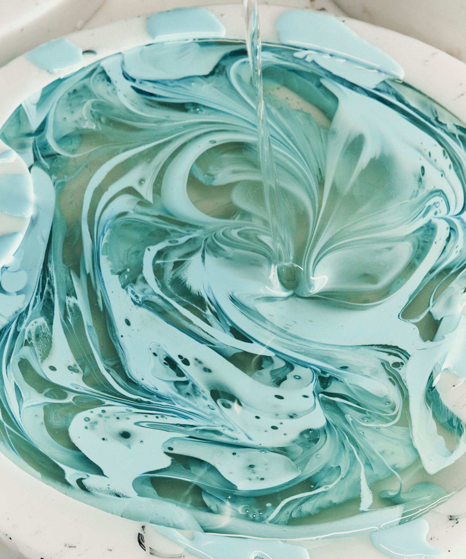 Marbled green and white resin being poured into a bowl