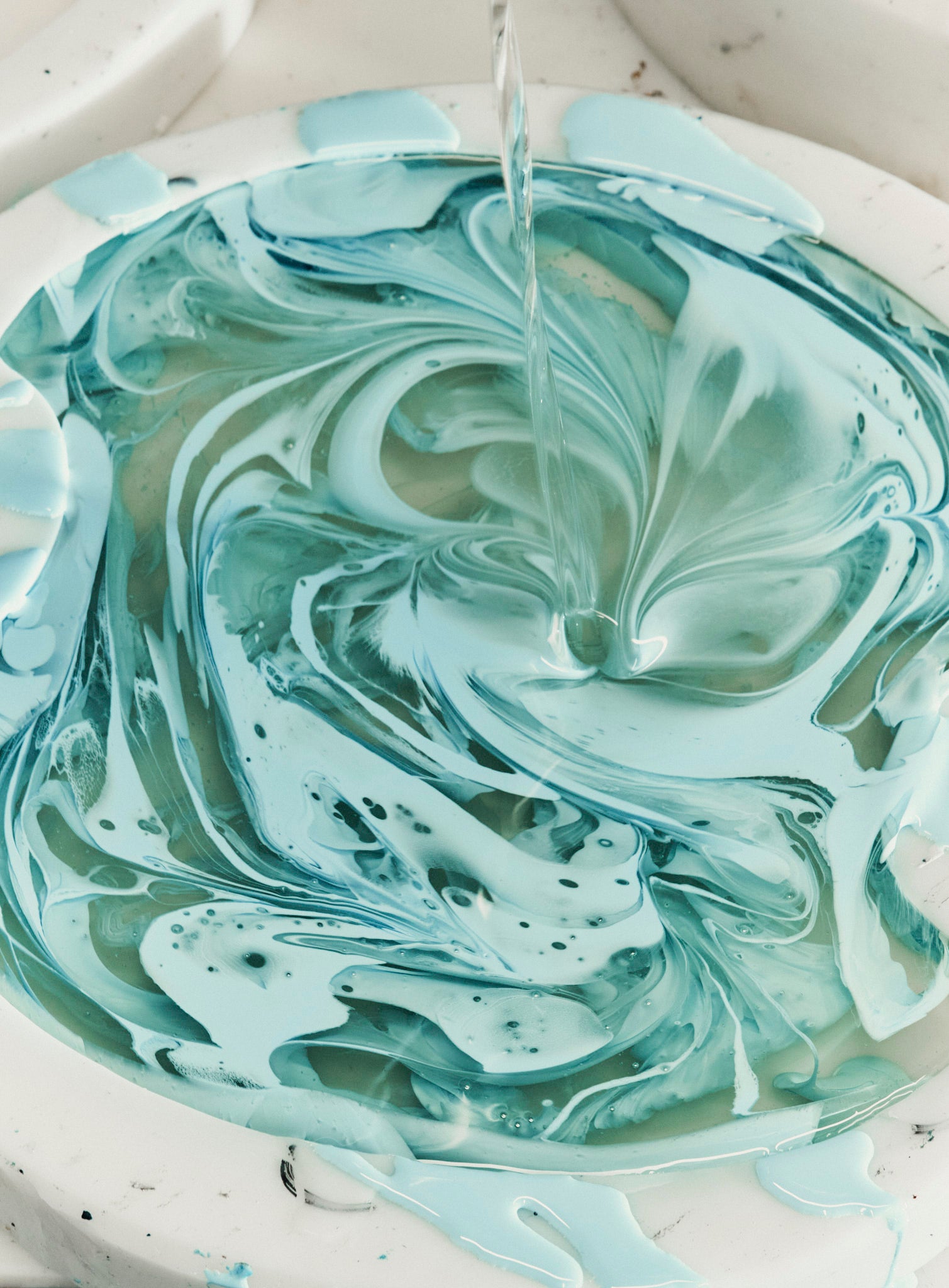 Marbled green and white resin being poured into a bowl