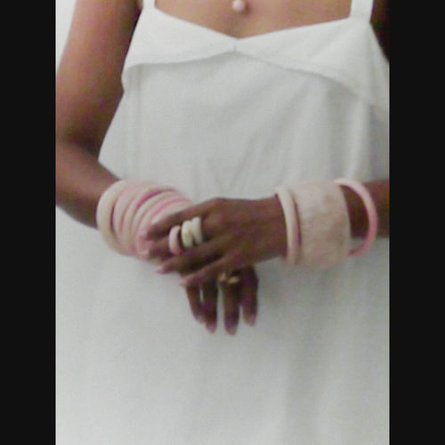 Model wearing variety of pink toned bangles with brass accent rings and pendants